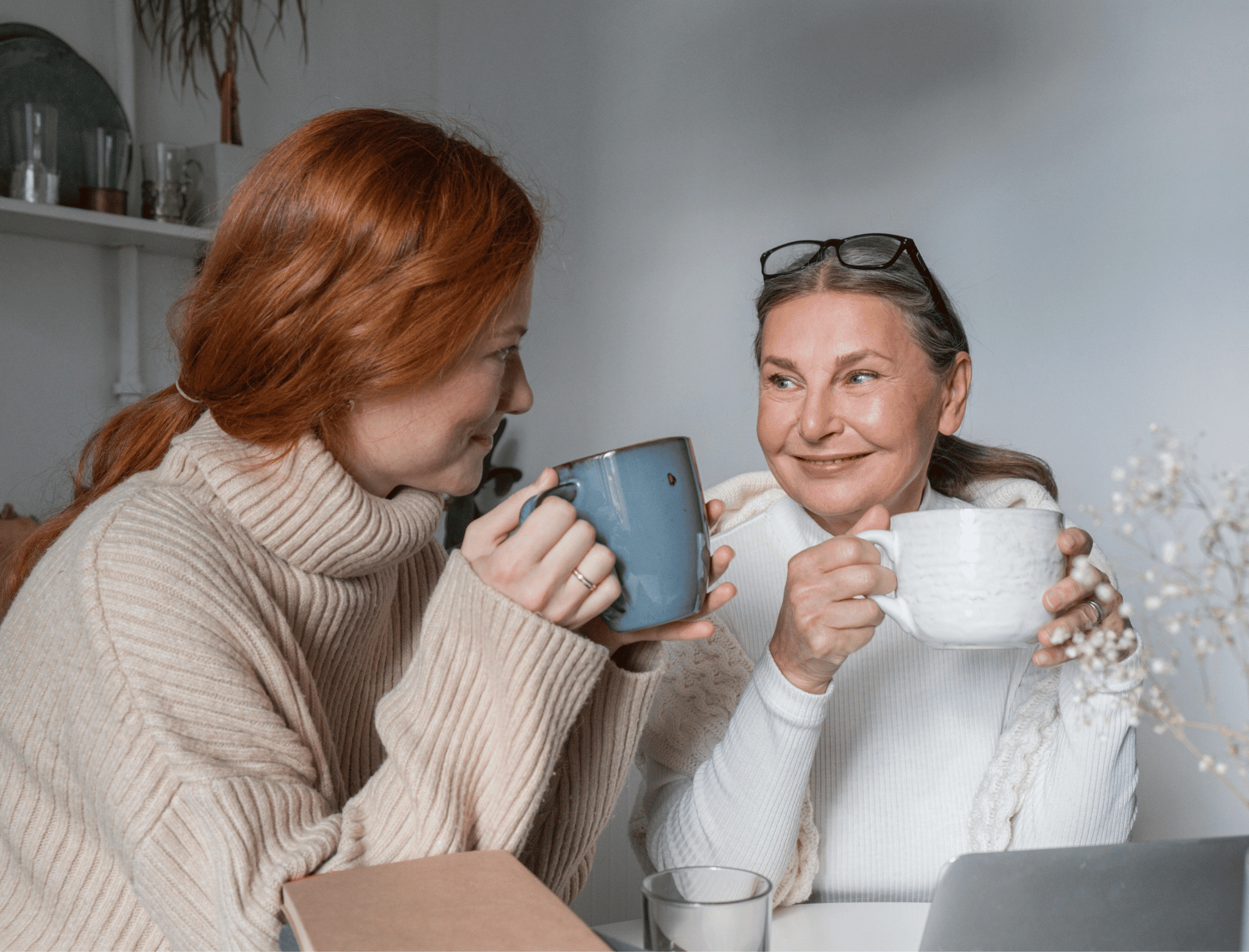 A daughter and mother smile and drink tea. Record family history with Safekeeping Stories.